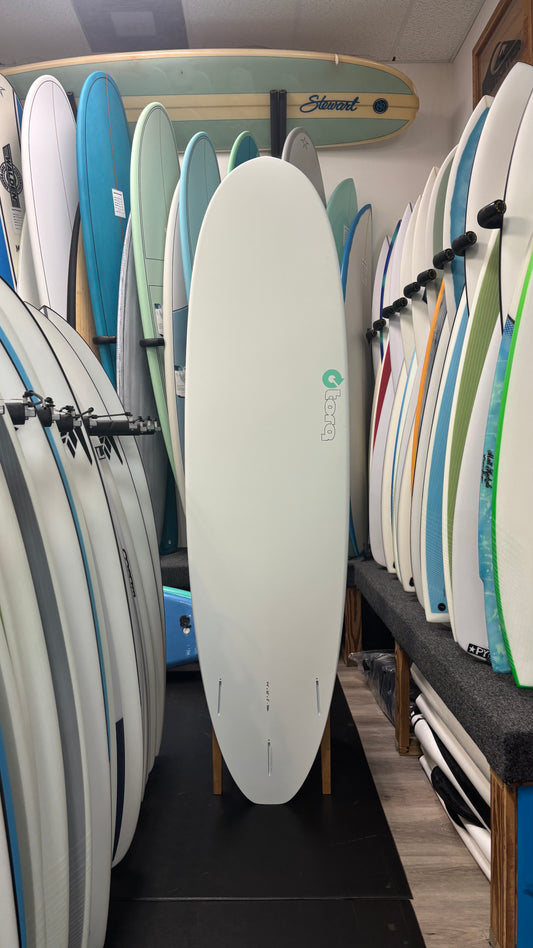 Row of surfboards in a store with a focus on a white surfboard.